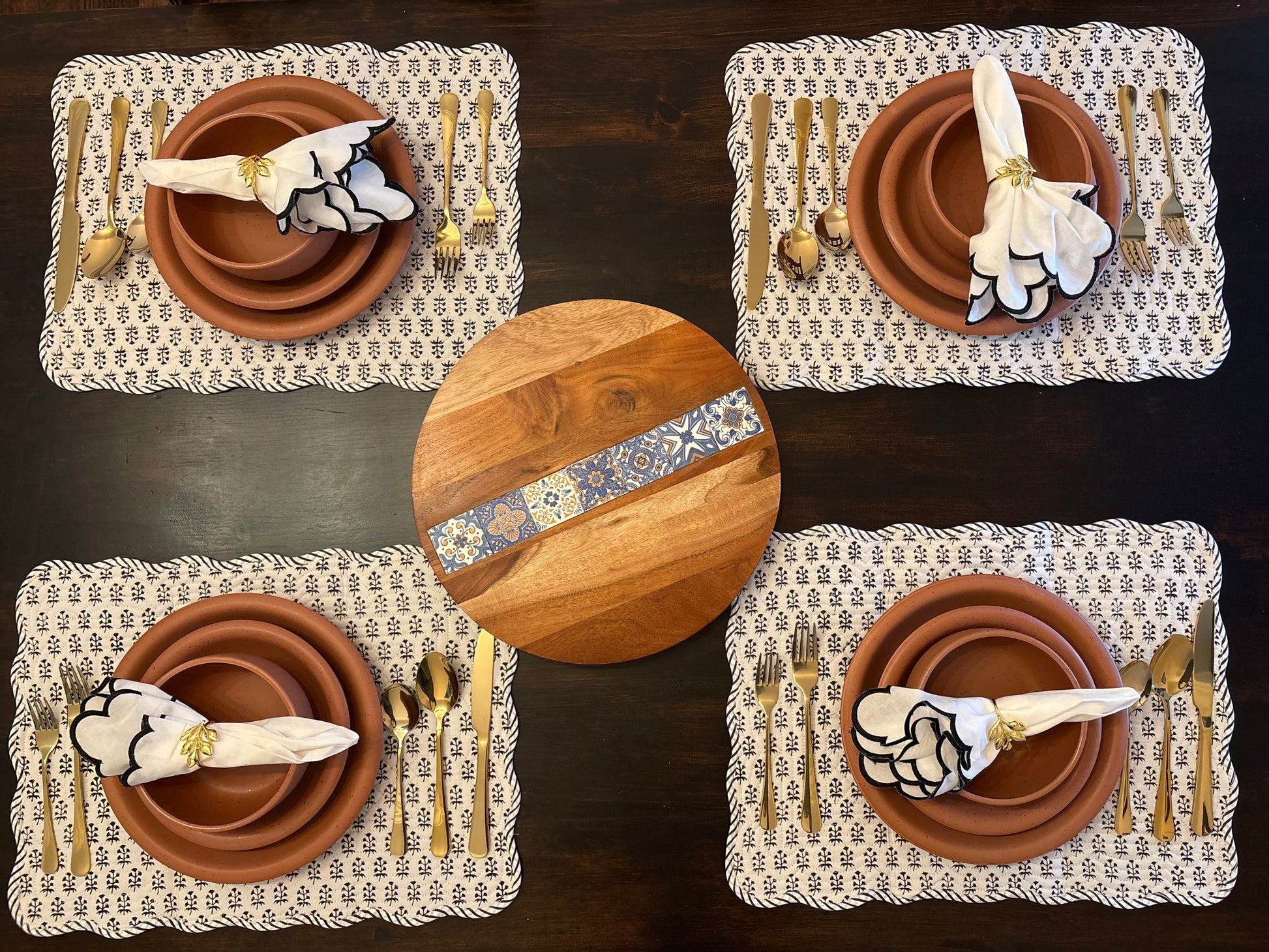 Set of four placemats with ceramic plates, cutlery, and a wooden board on a dark surface.